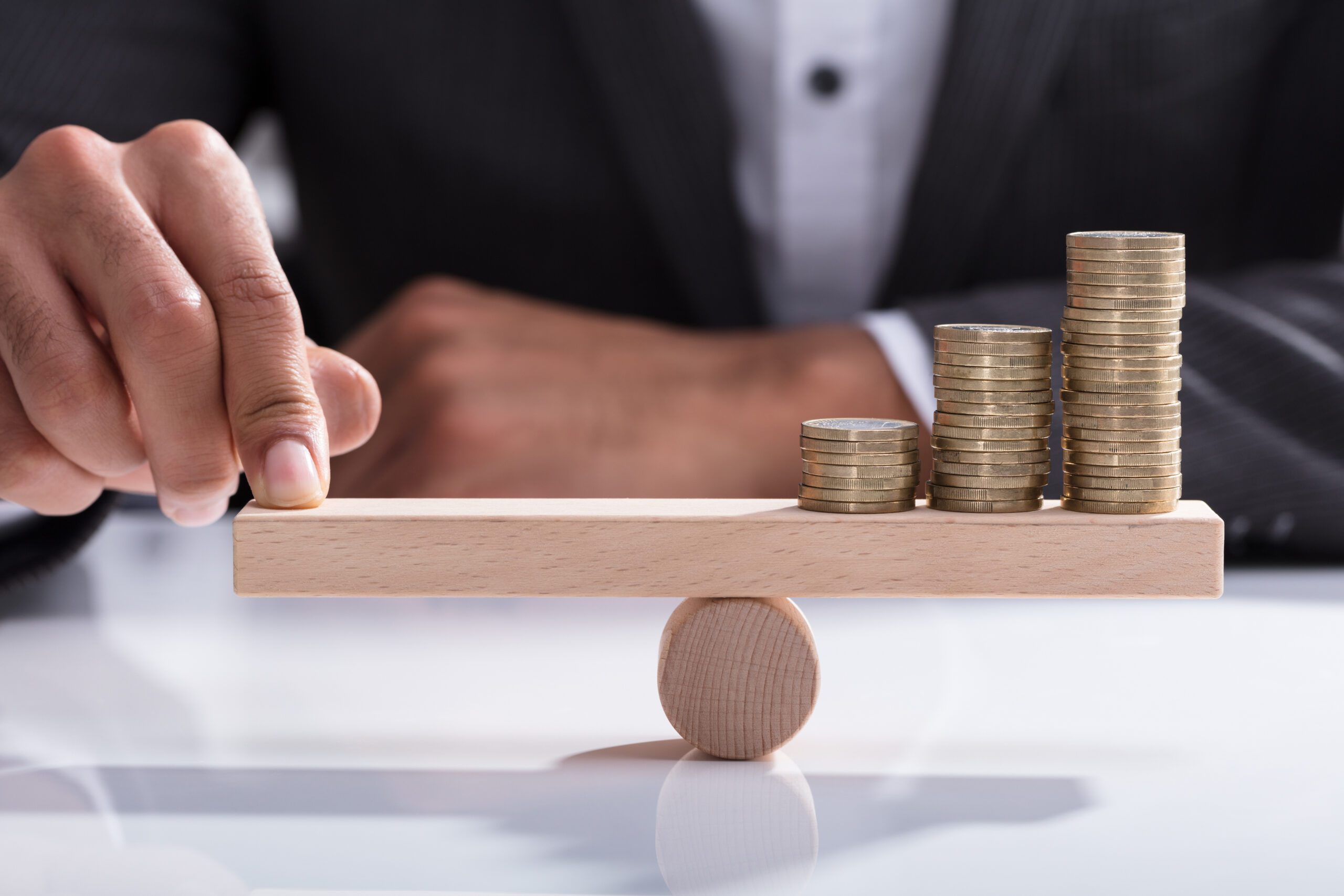 Businessperson Balancing Stacked Coins On Wooden Seesaw